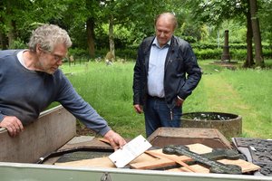 Pastor und Kunstschmied betrachten ein Grabkreuz und eine Tafel